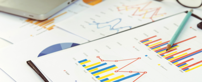 Graphs on a desk with a pair of glasses and laptop