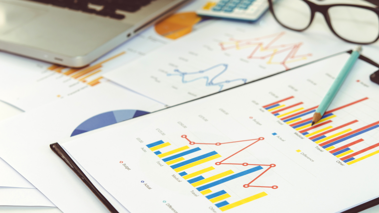Graphs on a desk with a pair of glasses and laptop